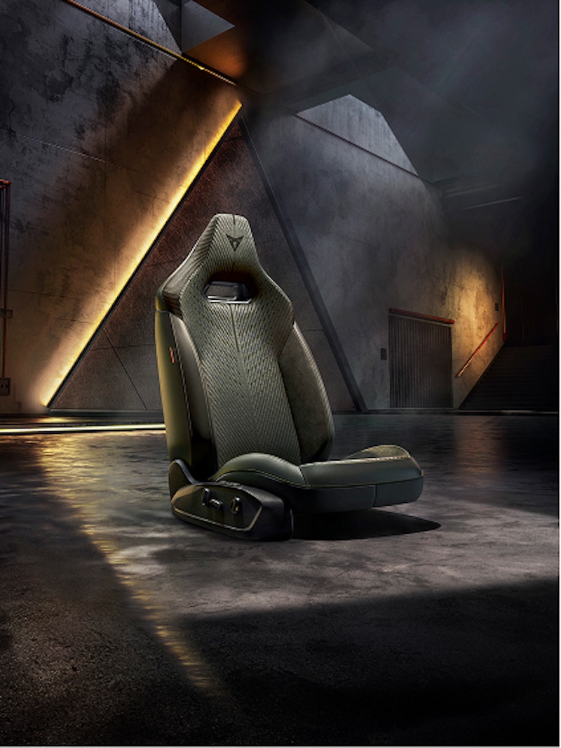 CUPRA Performance-Sitz freigestellt in einer dunklen Industriekulisse mit warmen Lichtreflexen auf dem Boden