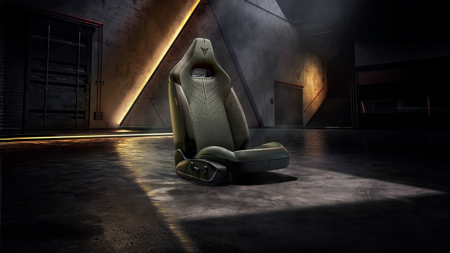 CUPRA Performance-Sitz freigestellt in einer dunklen Industriekulisse mit warmen Lichtreflexen auf dem Boden