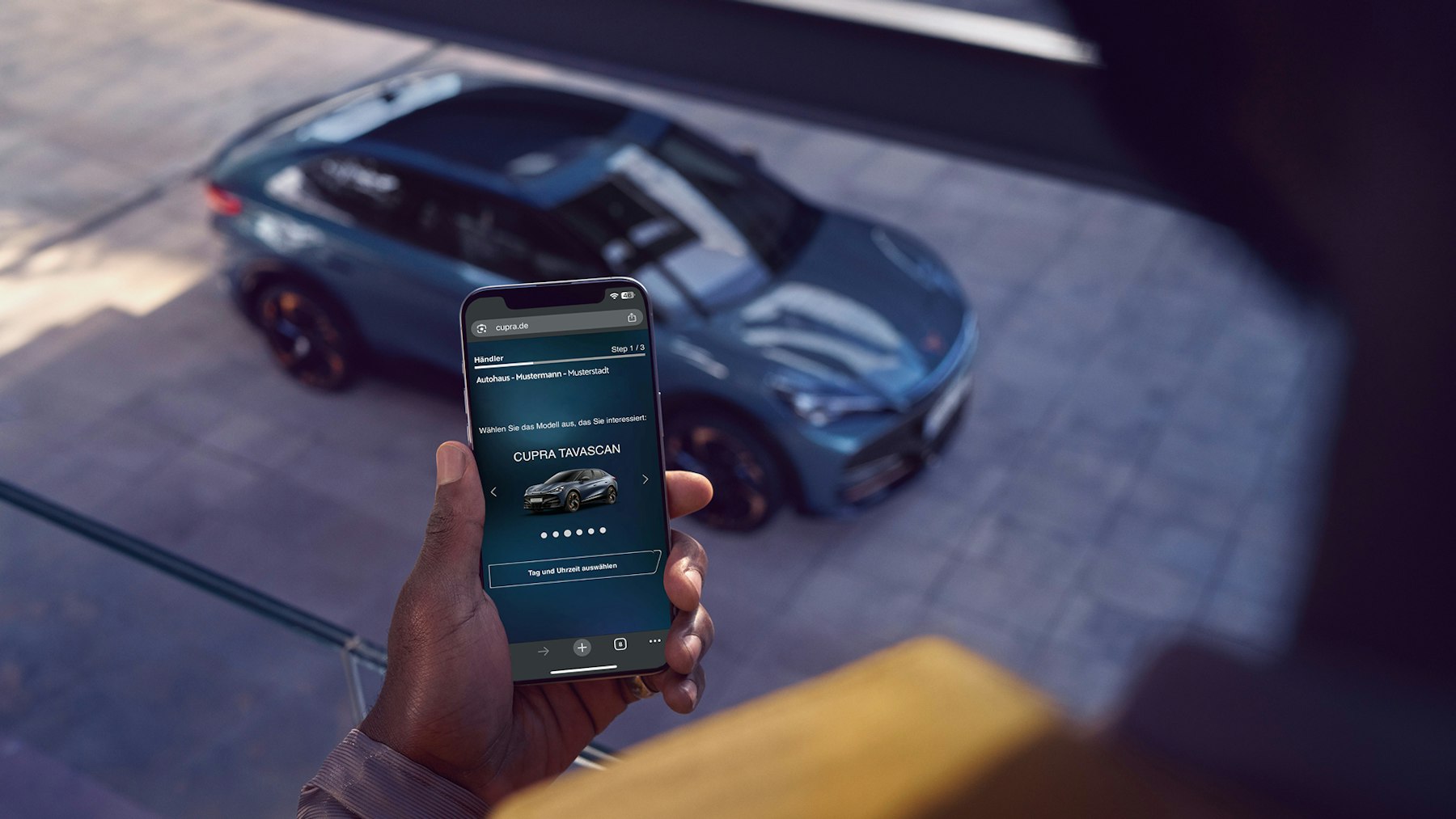 CUPRA Tavascan von schräg oben mit Person im Vordergrund, die eine Probefahrtbuchung am Smartphone tätigt