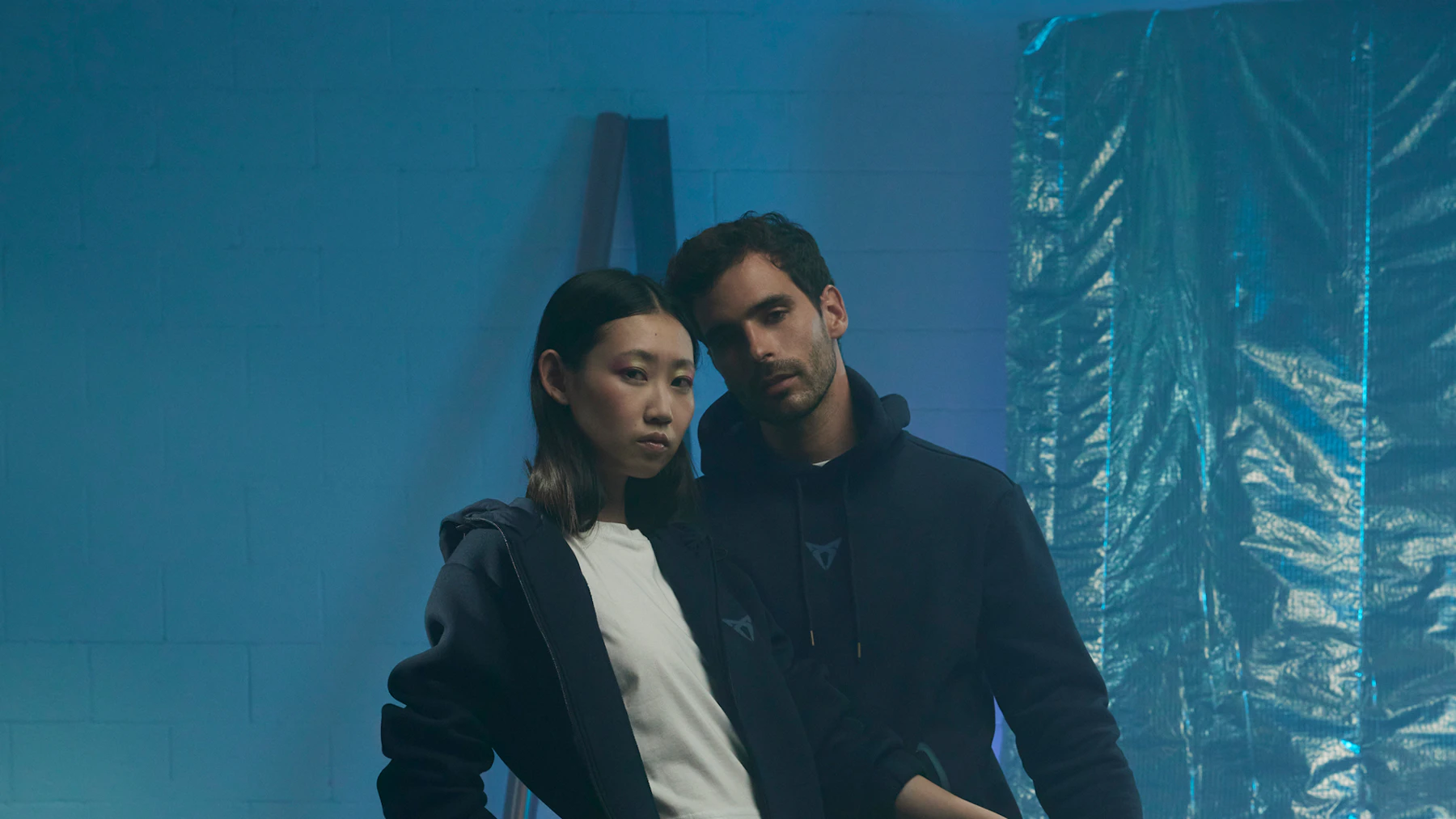 Zwei Personen in CUPRA Collection Kleidung, Hoodie in Dunkelblau mit CUPRA Logo